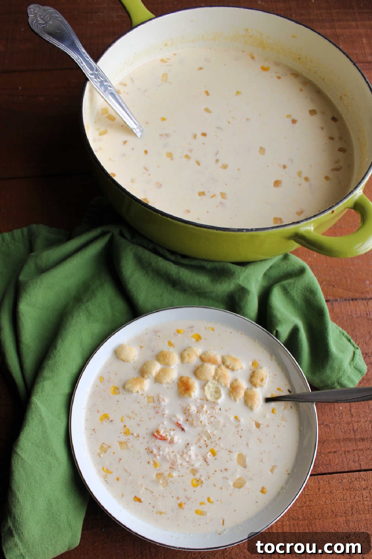 A large pot of creamy, spicy crab soup simmering on the stove next to a beautifully plated bowl of the same chowder, ready for serving.