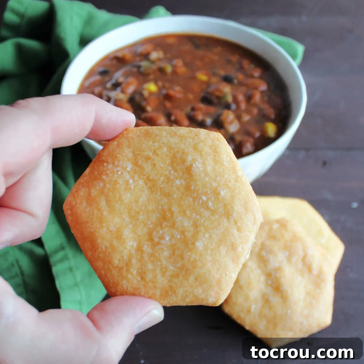 Hand holding cheese cracker in front of bowl of chili.