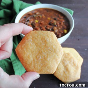 Hand holding cheese cracker in front of bowl of chili.