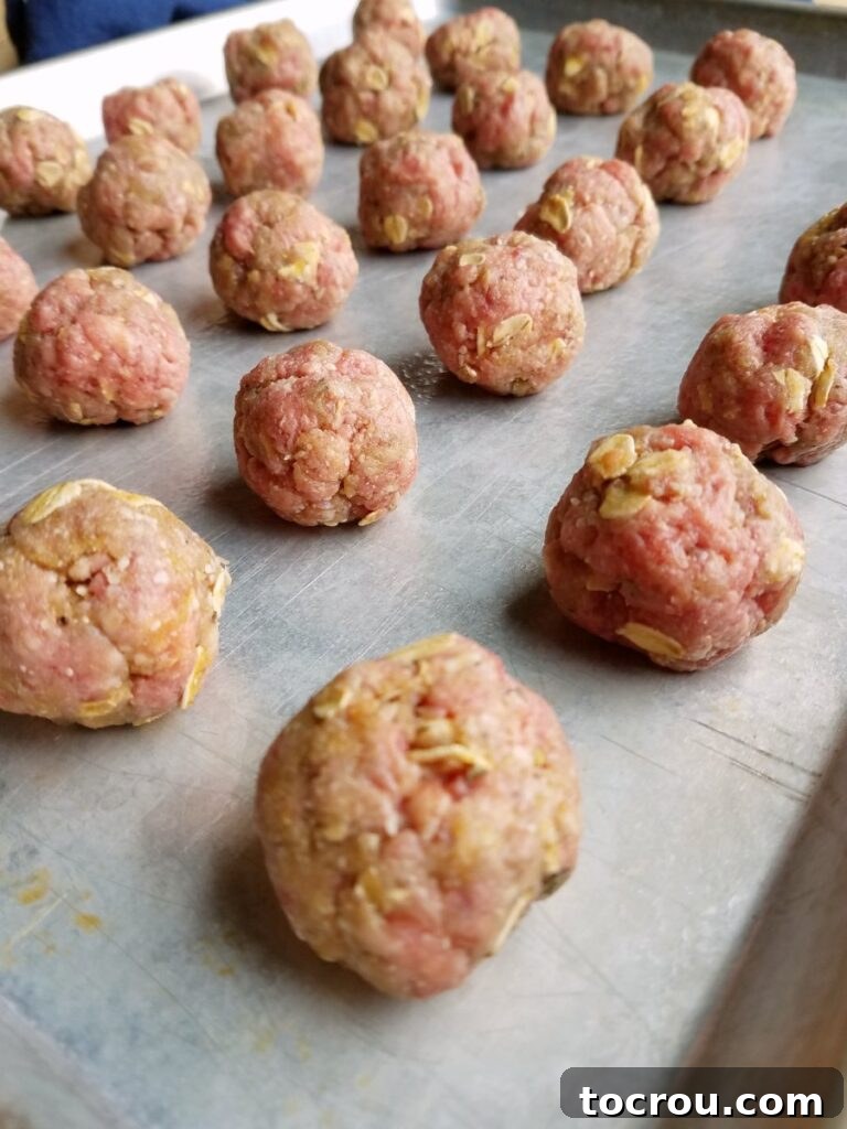 Sheet pan with rows of raw beef and oatmeal meatballs, perfectly formed and ready to bake.