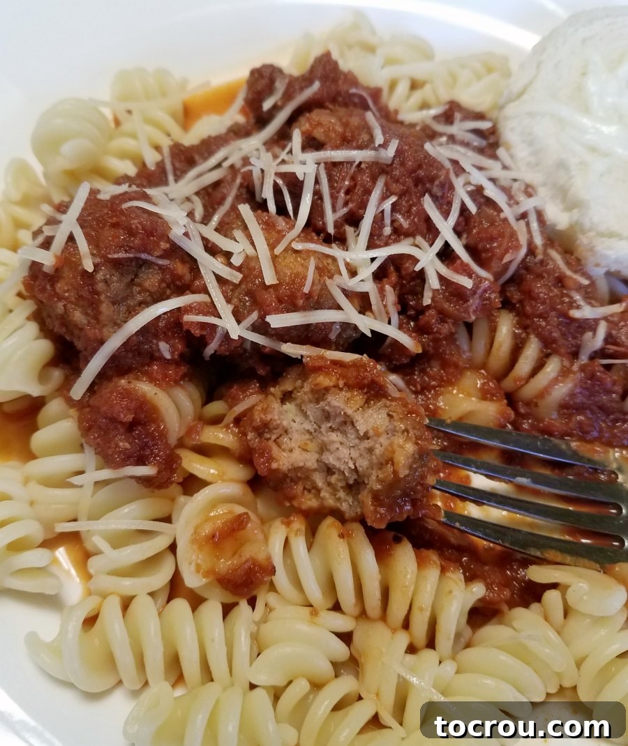 Fork in half of a meatball with tomato sauce and pasta, showing the tender texture and delicious interior.
