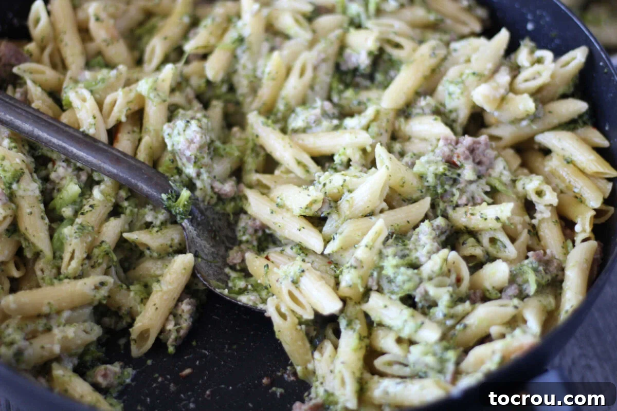 Pan of creamy pasta with broccoli and crumbled Italian sausage, garnished with fresh herbs.