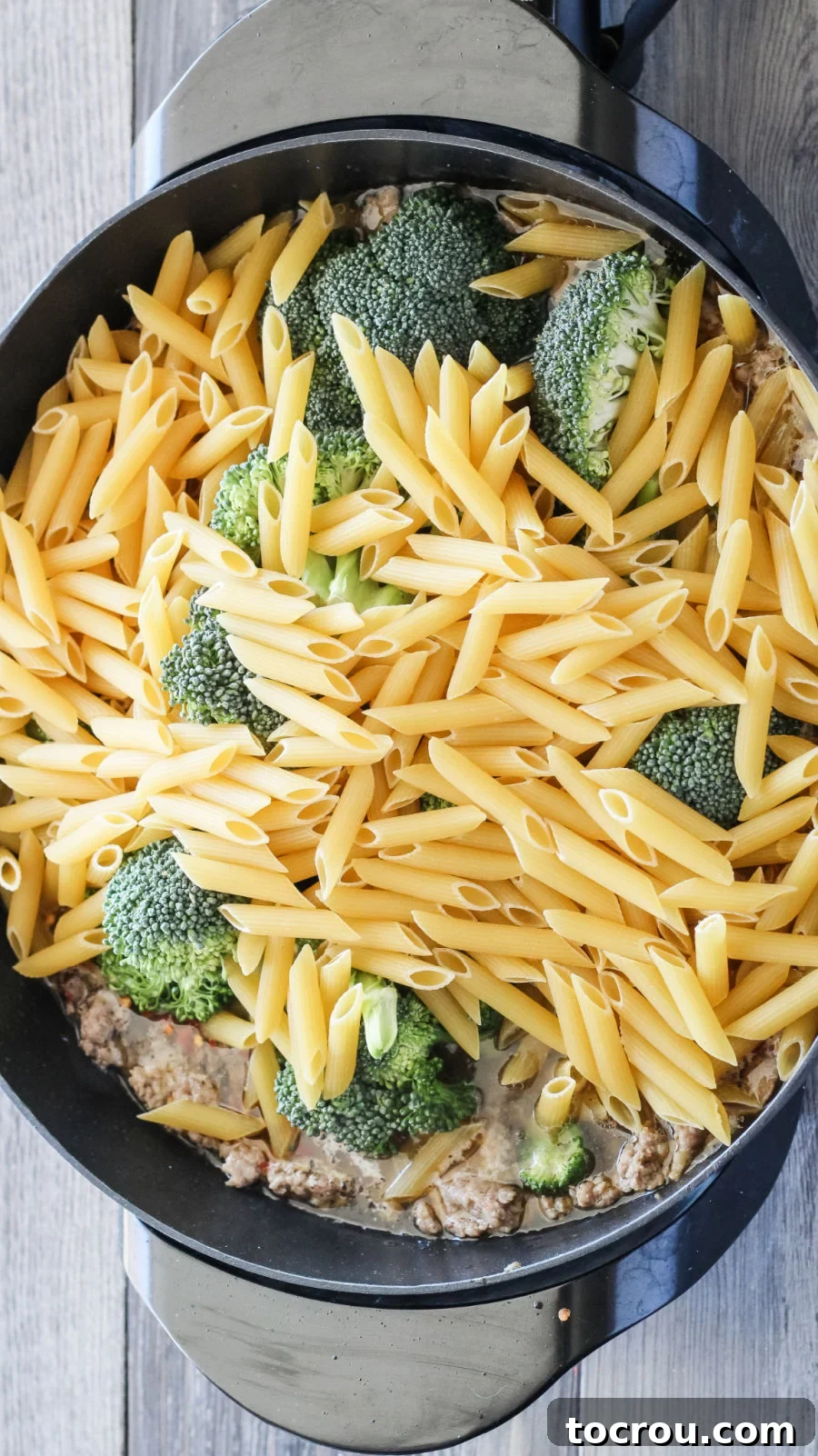 Adding pasta and broccoli to the pot with browned Italian sausage and chicken stock.