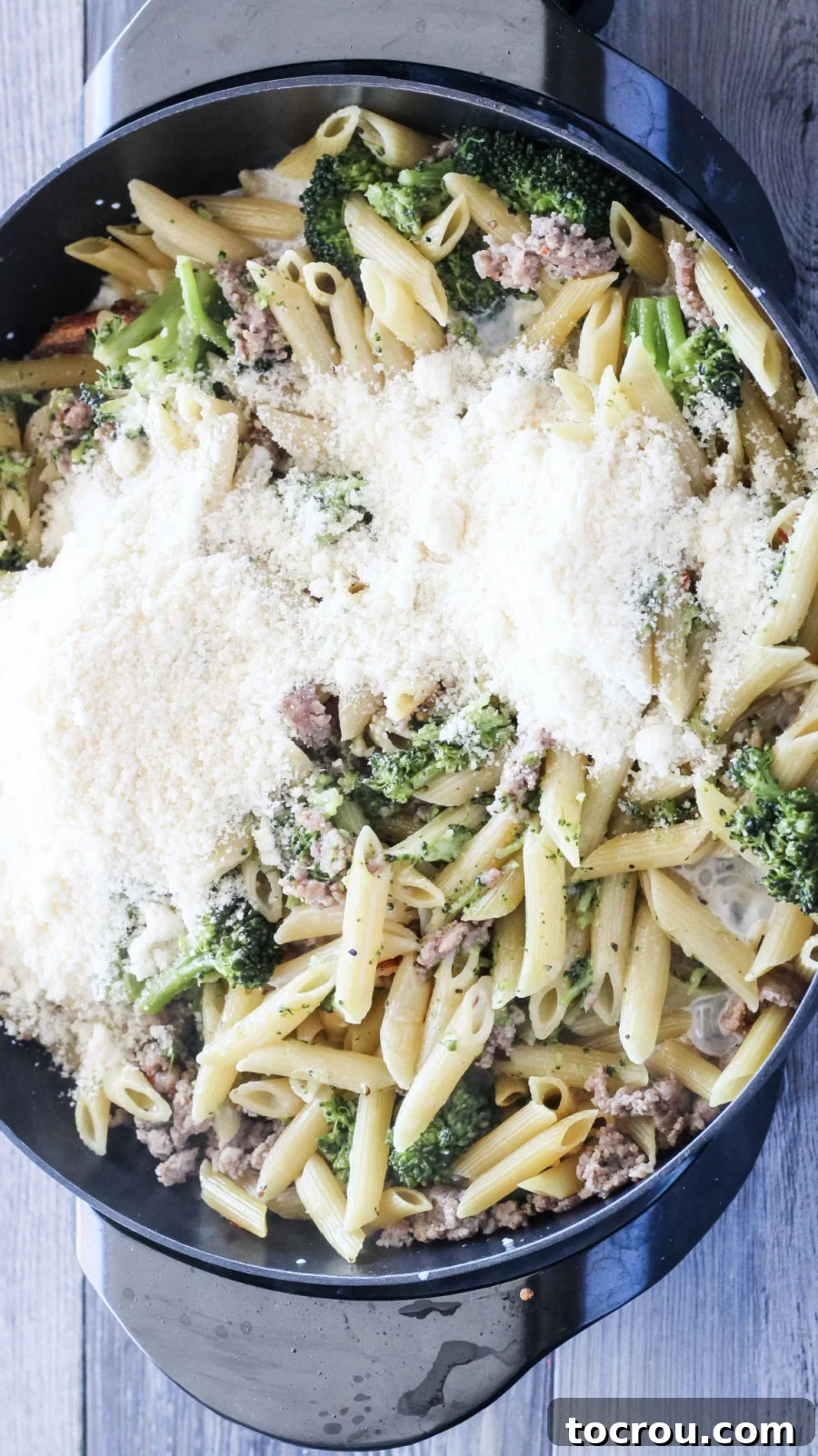 Adding grated Parmesan cheese to the one-pot sausage pasta, creating a creamy finish.