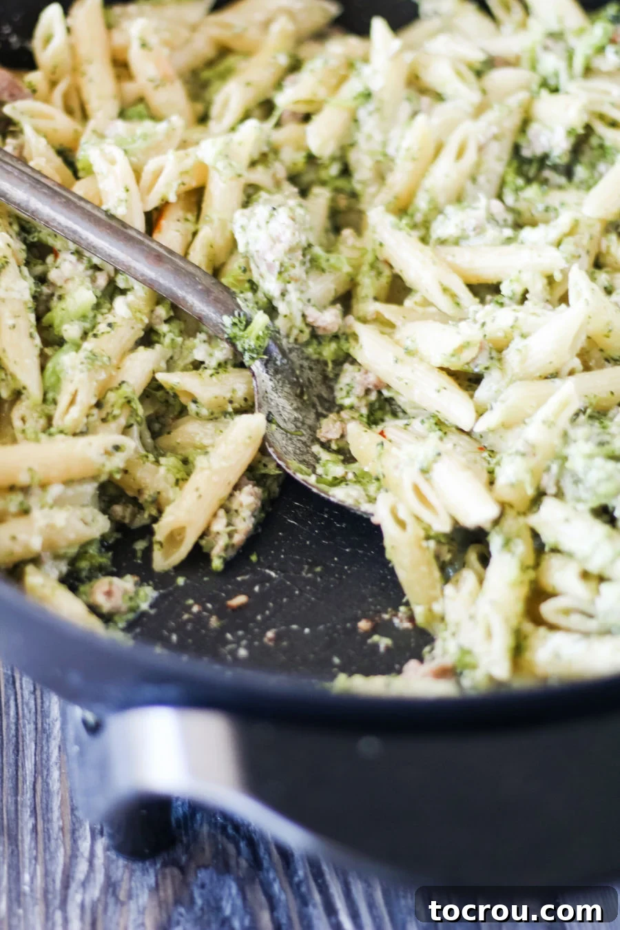 Pot full of creamy pasta with Italian sausage and broccoli, steaming and ready to be served.